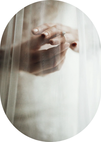 Zbliżenie dłoni delikatnie splecionych pod prześwitującą woalką, z miękkim ostrości. Obraz oddaje spokojną i intymną atmosferę ślubu.